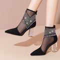 Black mesh ankle boots with crystal embellishments on a beige background