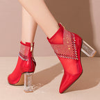 Red high-heeled ankle boots with clear heel and rhinestone details on a beige background
