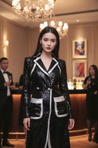Woman in a black and white dress standing in an elegant indoor setting with chandeliers.
