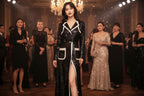 Woman in a black and white dress standing in a glamorous setting with other people.
