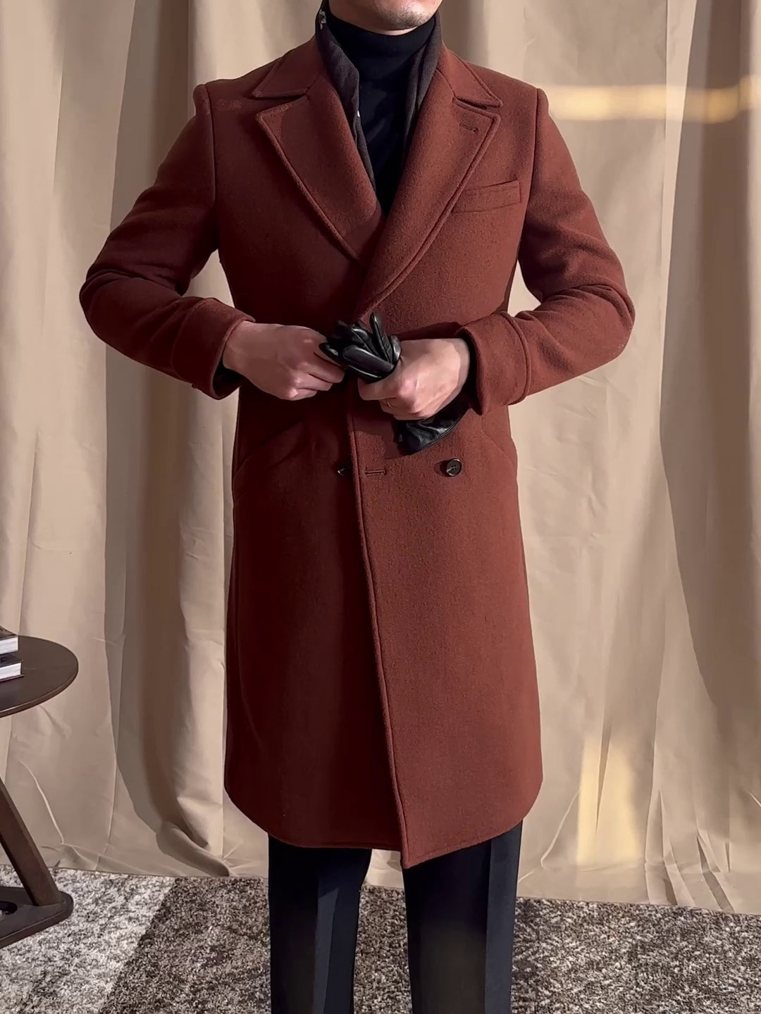 Person wearing a brown coat standing against a neutral background