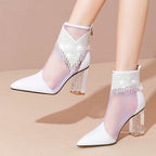 White high-heeled shoes with sheer mesh and crystal details on a beige background